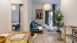 Un salon moderne avec un canapé, une table à manger dressée pour deux personnes, une plante en pot et une grande fenêtre avec des rideaux.