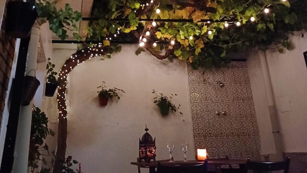 Un'area pranzo all'aperto con luci a catena, piante e un muro rustico.