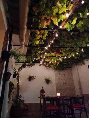 An outdoor dining area with string lights, greenery, and a rustic wall.