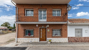 Un edificio in mattoni di due piani con un balcone, una porta in legno e un piccolo giardino fiorito.
