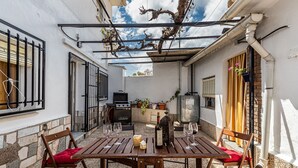 Un patio con tavolo e sedie di legno, un barbecue e piante in vaso.