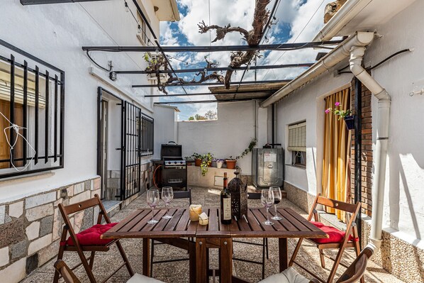A patio with a wooden table and chairs, a grill, and potted plants.