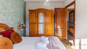 Una camera da letto con un letto, un armadio in legno e un bagno visibile attraverso una porta aperta.