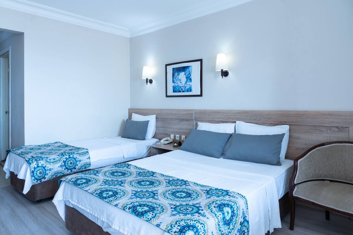 A hotel room with two beds, a chair, a nightstand, and a painting on the wall.