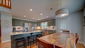 A modern kitchen with a central island, bar stools, and a dining table with chairs. - Creekfront Hayesville retreat w/ wrap-around porch and views! (Hayesville)