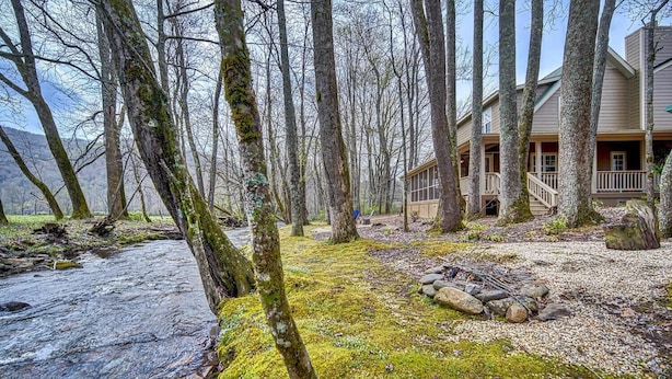 A cabin with a deck and a river in the foreground. - Creekfront Hayesville retreat w/ wrap-around porch and views! (Hayesville)