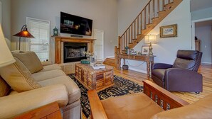 A living room with a fireplace, sofa, armchair, and a staircase. - Creekfront Hayesville retreat w/ wrap-around porch and views! (Hayesville)
