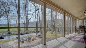 A covered outdoor area with a view of a river and trees. There are wooden chairs and a table. - Creekfront Hayesville retreat w/ wrap-around porch and views! (Hayesville)