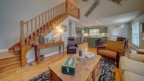 A spacious living area with a wooden staircase, a kitchen, and a dining area. - Creekfront Hayesville retreat w/ wrap-around porch and views! (Hayesville)