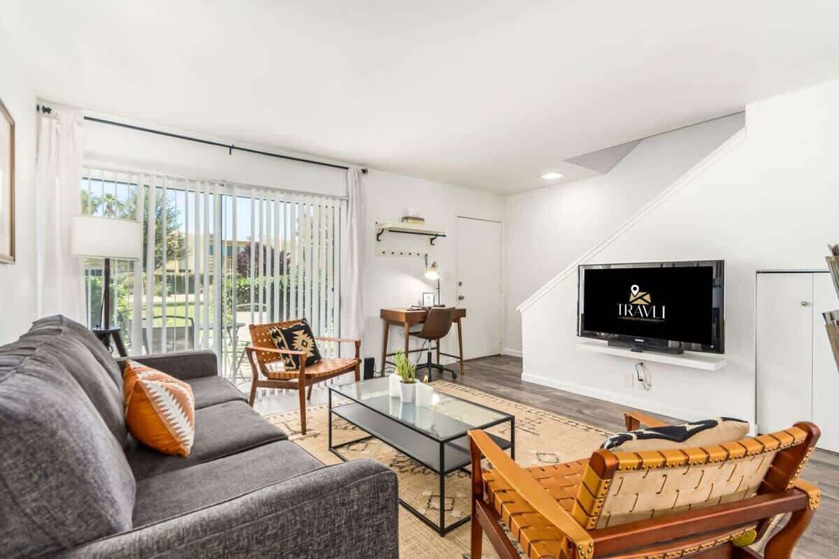 A modern living room with a sofa, chairs, a coffee table, a TV, and a view through large windows.