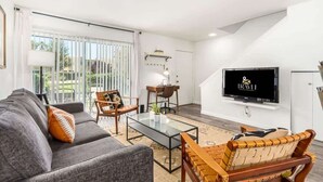 A modern living room with a sofa, chairs, a coffee table, a TV, and a view through large windows. - Camelback 446 | Walk 2 Old Town | 4 Pools (Scottsdale)