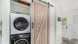 A laundry area with stacked washers and dryers, a sliding barn-style door, and a bathroom with a 'WELCOME' sign. - Camelback 446 | Walk 2 Old Town | 4 Pools (Scottsdale)