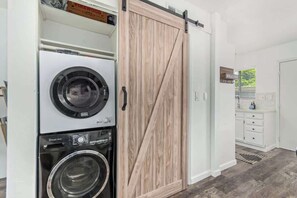 A laundry area with stacked washers and dryers, a sliding barn-style door, and a bathroom with a 'WELCOME' sign. - Camelback 446 | Walk 2 Old Town | 4 Pools (Scottsdale)