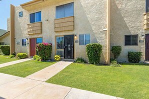 A two-story building with a beige stucco exterior, numbered 4610 and 446, featuring a front door, windows, and a small garden area with shrubs and flowers.