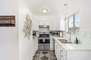 A modern kitchen with white cabinets, stainless steel appliances, a welcome sign, and a window with blinds.