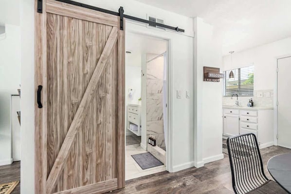 A modern kitchen with white cabinets, a black chair, and a sliding barn-style door leading to a bathroom.