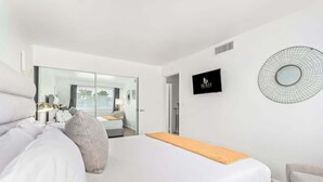 A modern hotel room with a large bed, a TV, a mirror, and a view into the adjacent room. - Camelback 446 | Walk 2 Old Town | 4 Pools (Scottsdale)