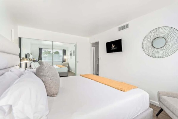 Une chambre d’hôtel moderne dotée d’un grand lit, d’une télévision, d’un miroir et donnant sur la chambre voisine.