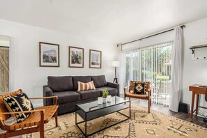Un salon comprenant un canapé, deux fauteuils, une table basse et une grande fenêtre avec des rideaux.