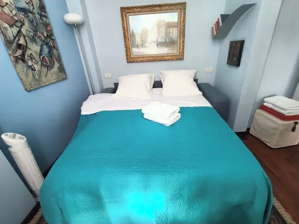 A neatly made bed with a teal bedspread and white pillows in a room with light blue walls.