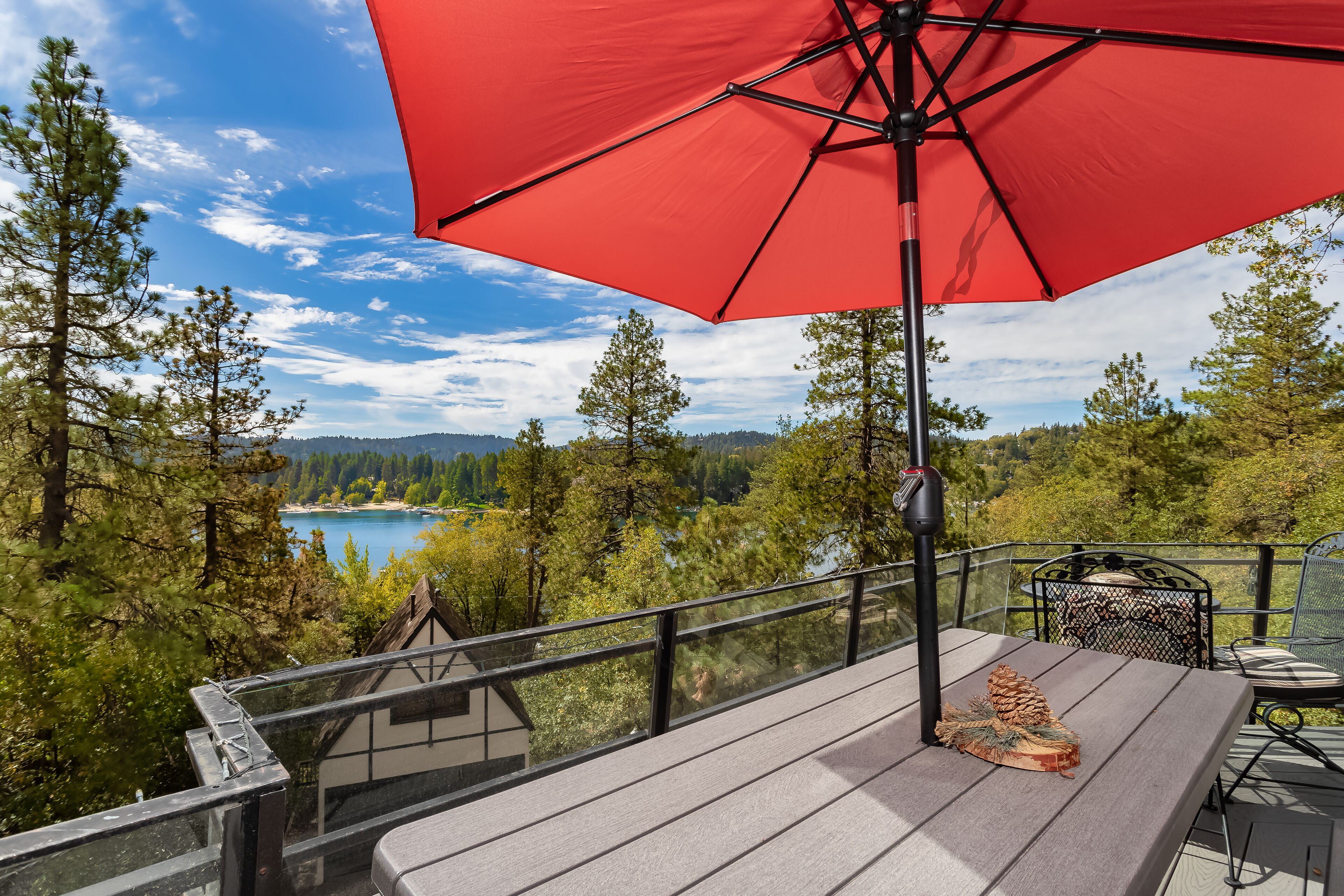 Une terrasse avec un parasol rouge, donnant sur un lac et une zone boisée.