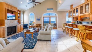A spacious living room with a fireplace, a television, and a large window overlooking the ocean. - Blue Heron - Dog Friendly, Community Pool, Across from Beach, Sunset Beach! (St. George Island)
