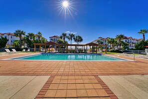 Una piscina con solárium empedrado, palmeras y un cielo azul despejado.