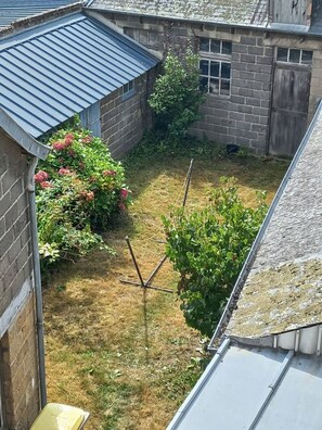 A courtyard with a brick wall, a metal roof, and a small garden area with plants and a wooden structure.