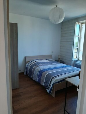 A bedroom with a bed, a bedside table, a hanging light fixture, and a window.