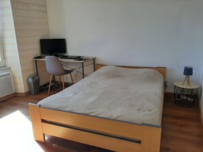 A bedroom with a bed, a desk with a computer, a chair, and a lamp.