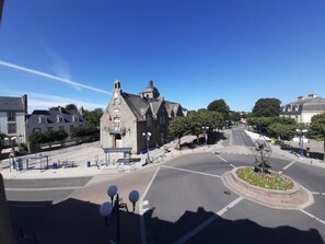 A street view with a roundabout, a historic building with a clock tower, and a clear blue sky.