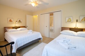 A hotel room with two beds, a ceiling fan, artwork on the walls, and a closet.