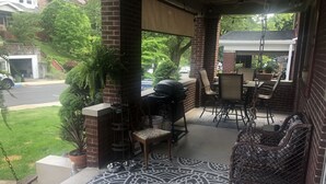 Una veranda coperta con pavimento decorato, arredi da esterno, un barbecue e una pianta in vaso.