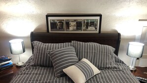 Un letto rifatto con biancheria a righe e cuscini, una cornice con foto sopra e due abat-jour ai lati.