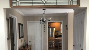 Un corridoio con pavimento in legno, un tappeto decorato, un lampadario e una cucina sullo sfondo.