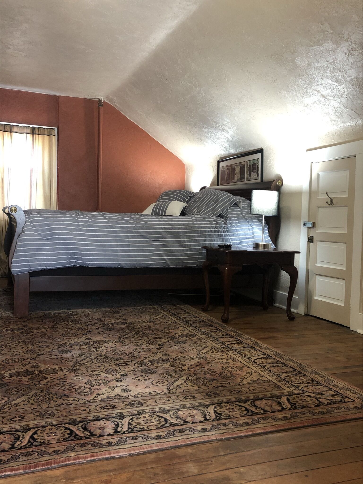 A bedroom with a bed, a nightstand, a door, and a patterned rug.