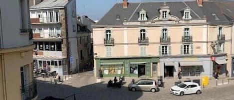 A square with buildings, a café, and parked cars.