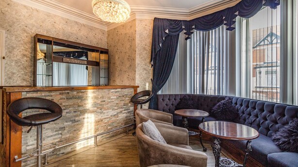 A bar area with a mirror, bar stools, and a seating area with a sofa and two round tables. - Cherry Tree House (Blackpool)