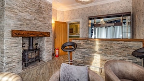A cozy room with a stone wall, a wooden bench, a bar area, and a large mirror. - Cherry Tree House (Blackpool)