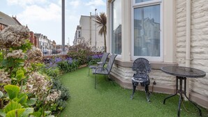 A garden with artificial grass, two metal chairs, and a small round table. - Cherry Tree House (Blackpool)