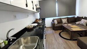 Et moderne køkken med vask, komfur og skabe. Der er et spiseområde med en sofa og et bord.