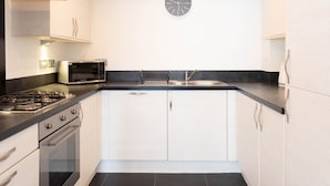 A modern kitchen with white cabinetry, a black countertop, a built-in microwave, a stove, and a sink.