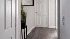 A hallway with a white door, a black floor lamp with a plant, and a ceiling light fixture.