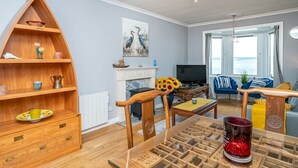Una sala de estar con una estantería de madera, una chimenea, un televisor y vista al mar.