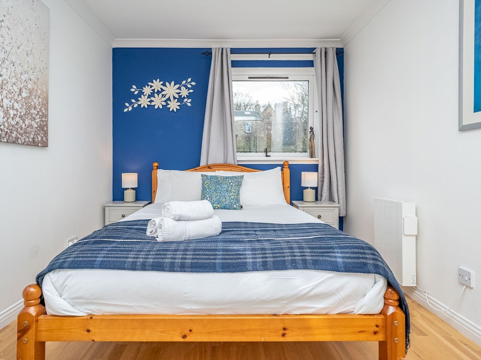 A neatly made bed with a blue and white checkered blanket, two pillows, and a folded towel on the side.
