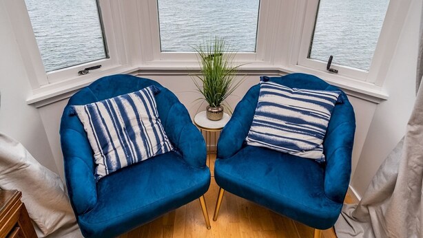 Habitación de esquina con dos sillones azules, una mesita con una planta y vista al mar a través de amplios ventanales.