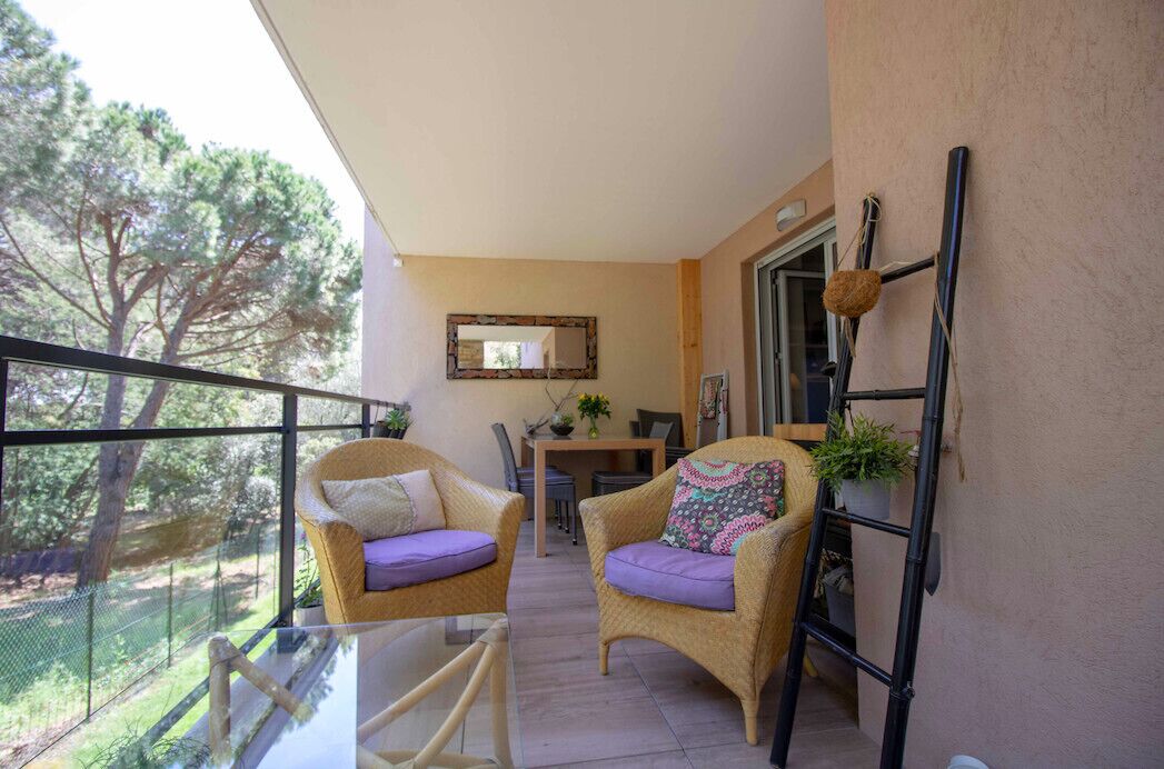 Un balcon avec des fauteuils en osier, une table en verre et une vue sur les arbres.