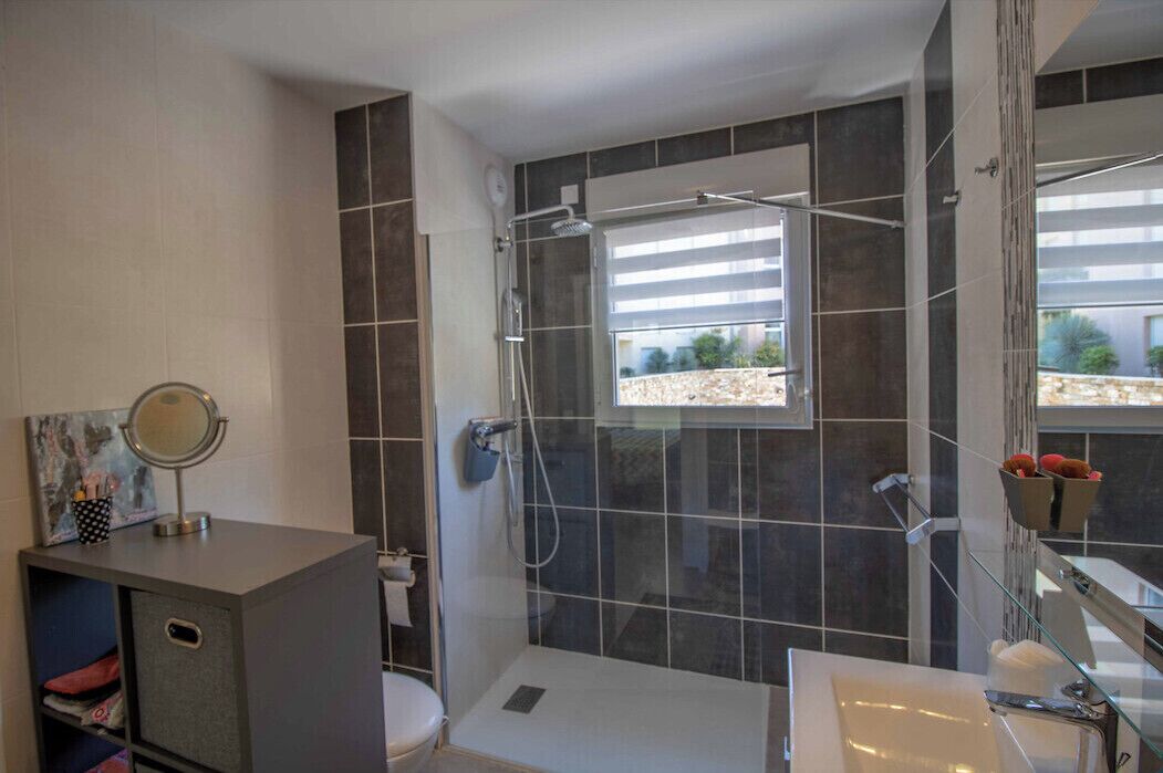A modern bathroom with a glass-enclosed shower, a vanity with a mirror, and a view of the outdoors through a window.