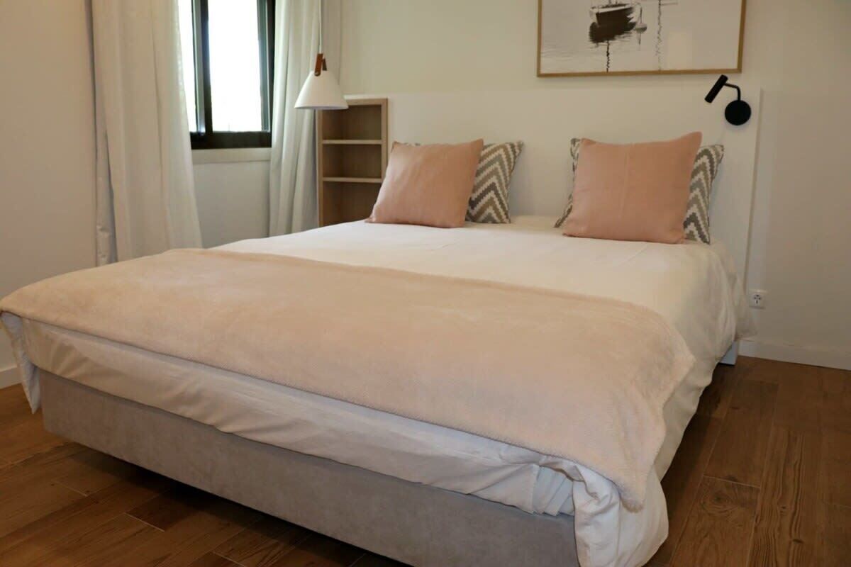 A neatly made bed with a light-colored duvet and pillows, a bedside lamp, and a wall-mounted shelf.