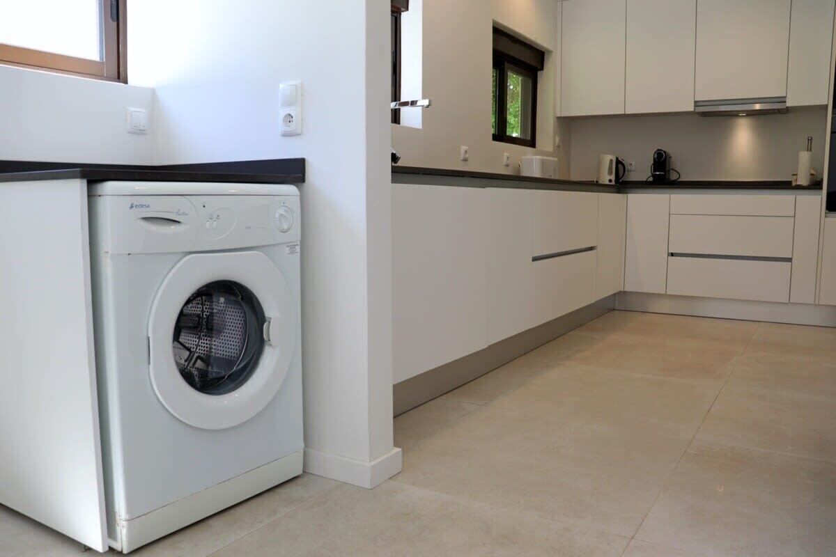 A compact kitchen with a built-in washer, a window, and a countertop with a kettle.